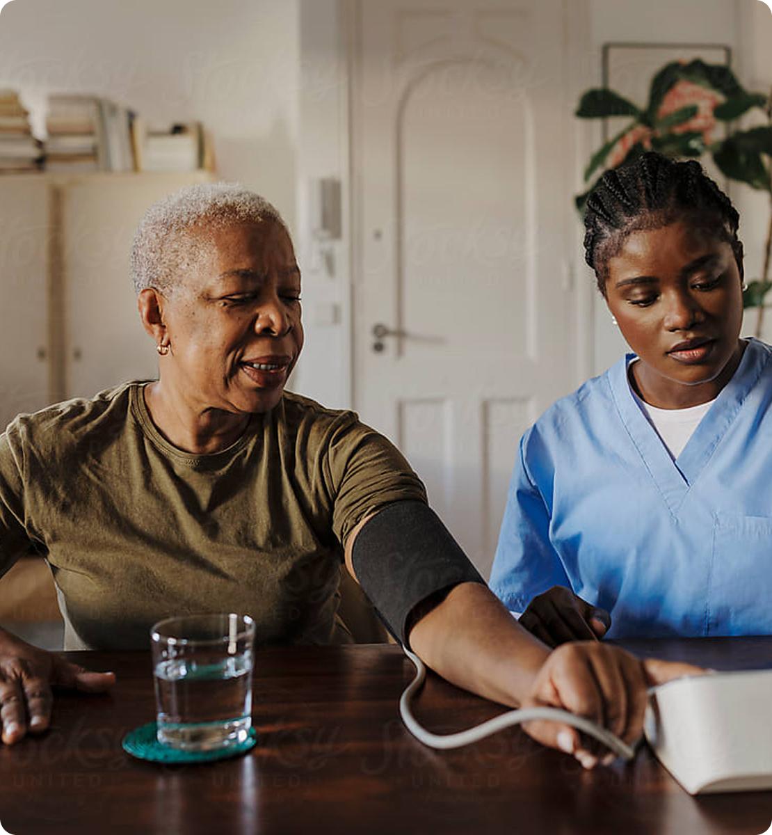 female nurse sitting at a table taking an older woman's blood pressure