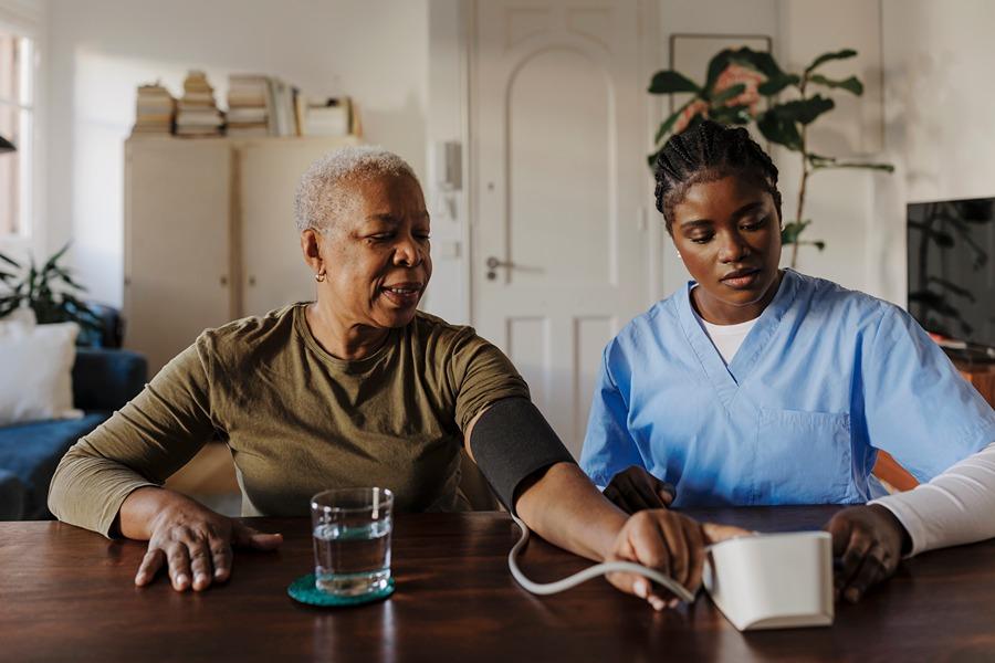 female nurse taking female patient's blood pressure while sitting at table
