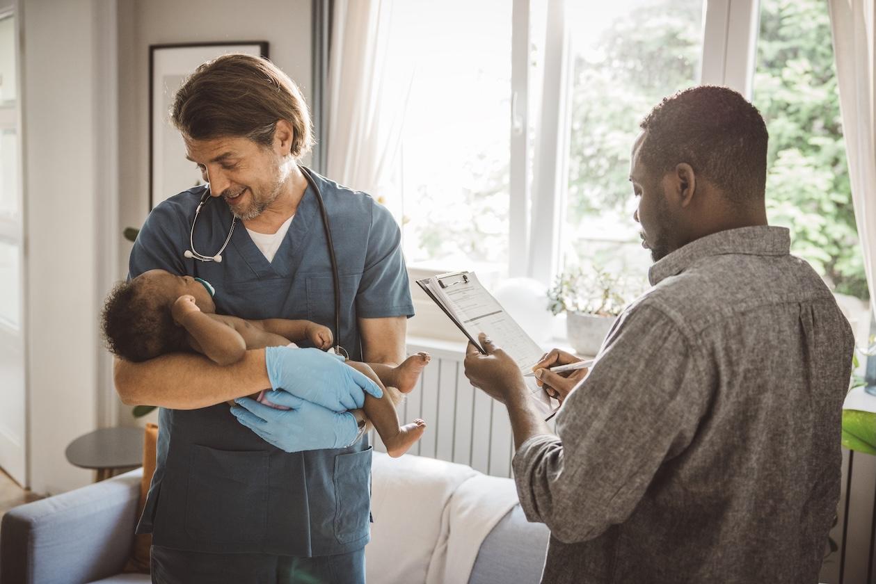 male nurse holding and smiling at baby while man writes on clipboard next to them