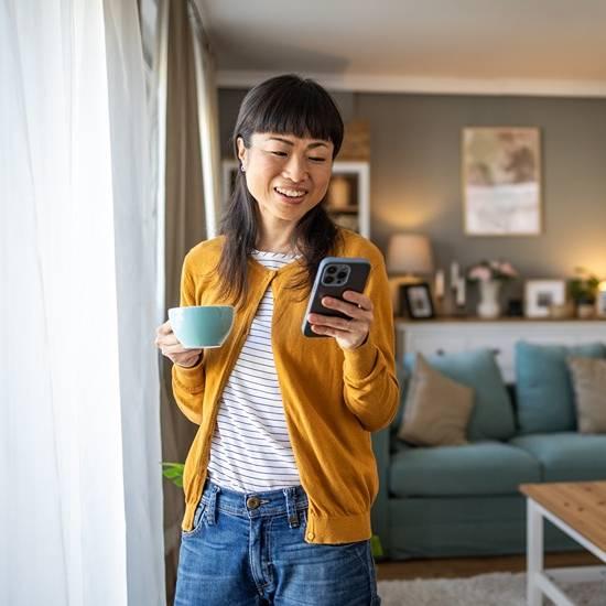 Woman smiling looking at her phone and holding a coffee cup