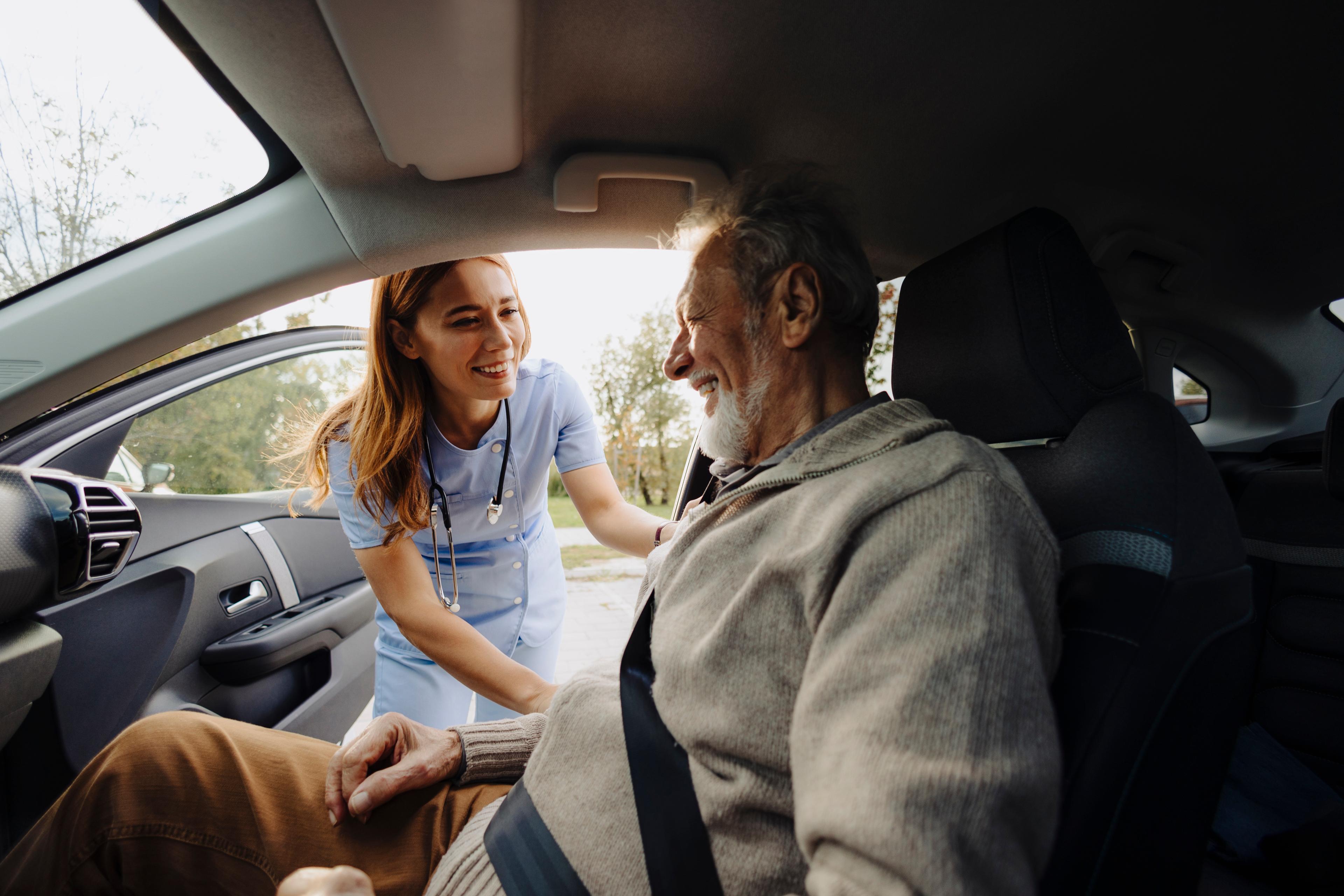 Female caregiver helping elderly man into car